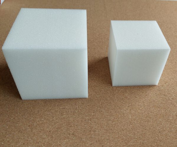 Achtergrond van kurk met op de voorgrond 2 schuimrubberen kubussen afgebeeld. Links 10 x 10 cm. Rechts 8 x 8 cm.